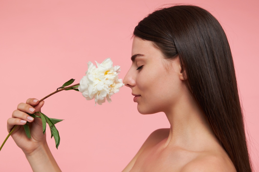 cute-looking-woman-with-closed-eyes-brunette-long-hair-and-healthy-skin-touching-nose-with-a-flower-smells-aroma-closeup-stand-isolated-over-pastel-pink-wall.jpg
